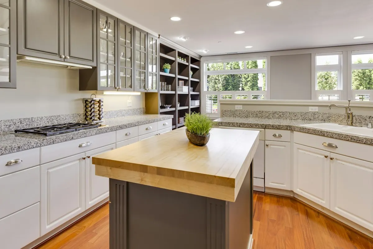 Kitchen with a butcher-block island, granite perimeter counters and white cabinets with glass uppers