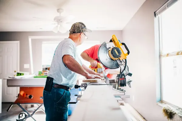 Carpenter cutting trim on a miter saw set up inside a house during a remodel