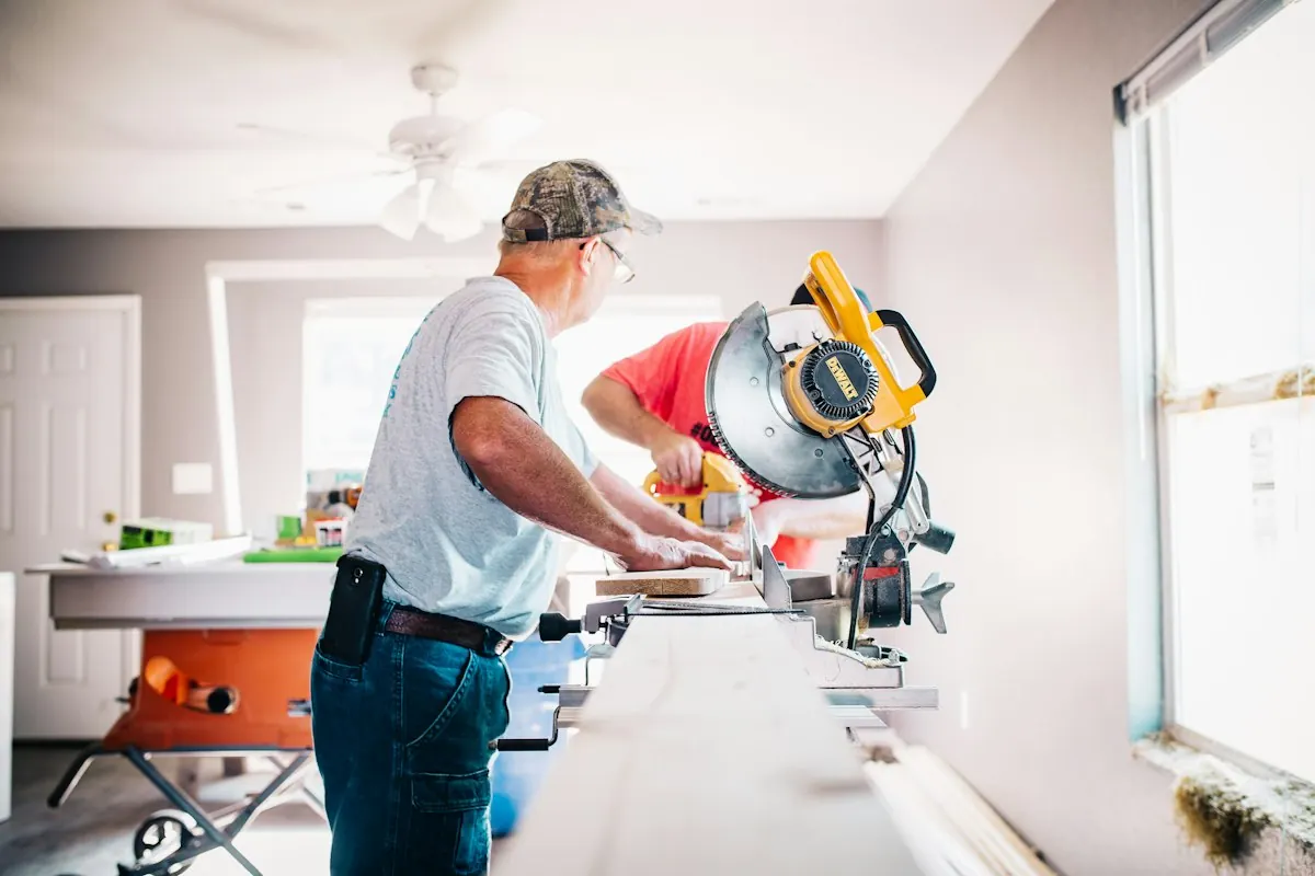 Carpenter cutting trim on a miter saw set up inside a house during a remodel