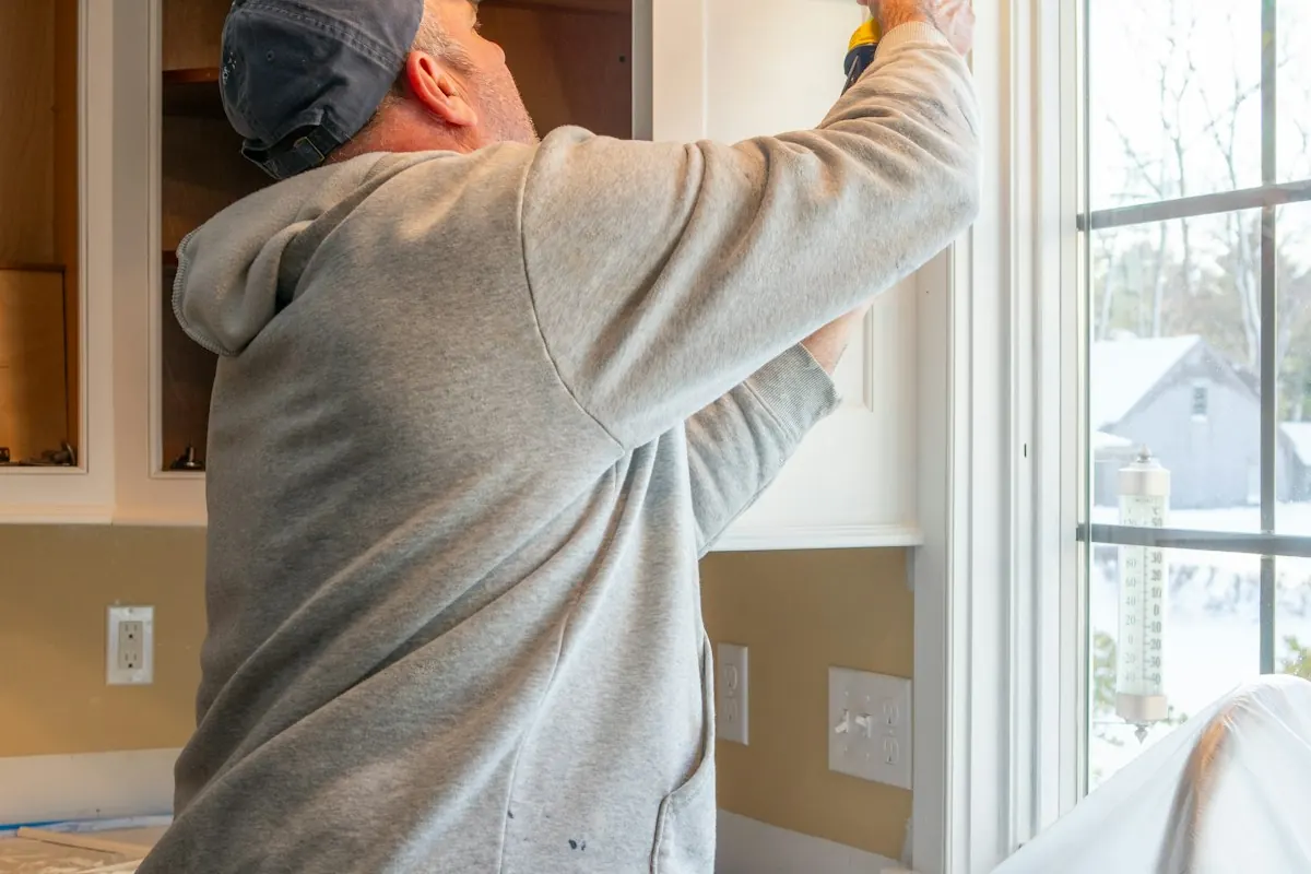Worker caulking a window frame in a kitchen with the counters covered in plastic