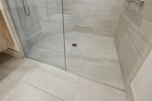 Curbless walk-in shower with large floor tiles, a glass panel and a floor drain, no step at the entry