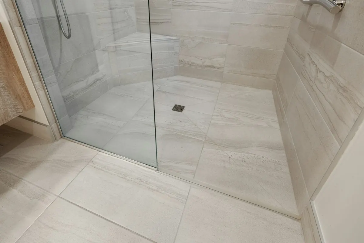 Curbless walk-in shower with large floor tiles, a glass panel and a floor drain, no step at the entry