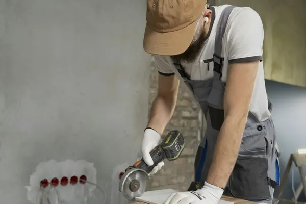 Tile setter cutting a tile with an angle grinder on a workbench