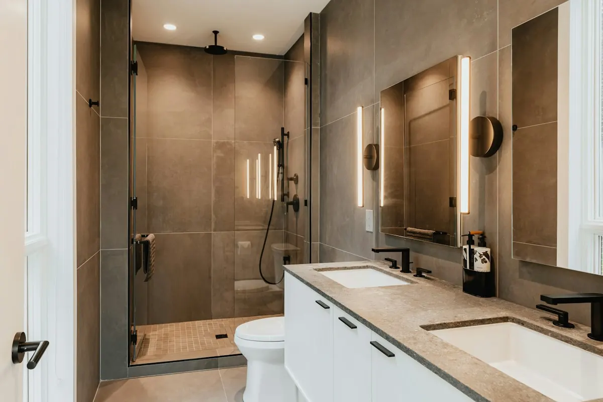 Walk-in shower in large dark porcelain tile with a glass door, beside a double vanity