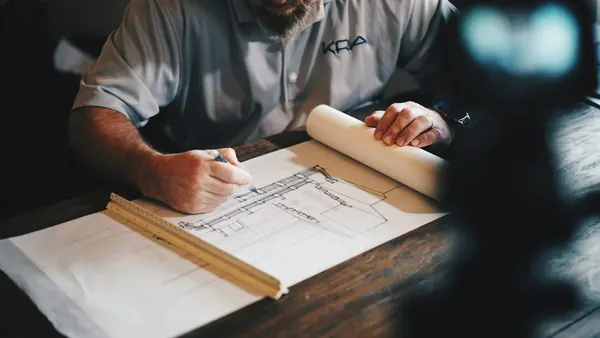Designer drafting a floor plan with a pencil and ruler at a table