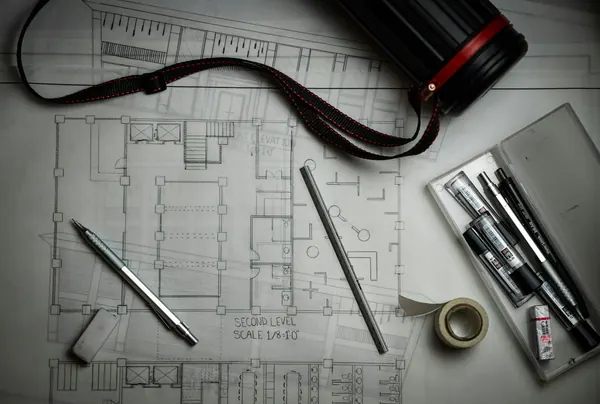 Printed floor plans with drafting pencils, a metal ruler and a plan tube