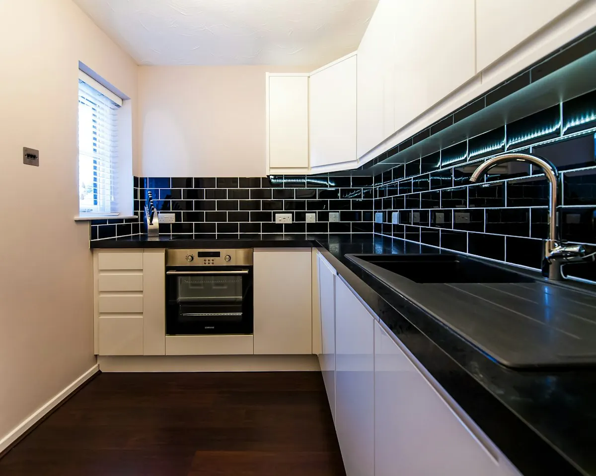 Narrow galley kitchen with white cabinets, black subway tile and a wall oven
