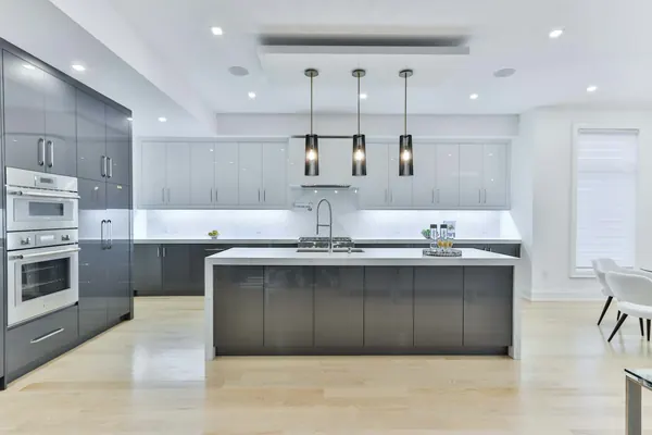 Kitchen with tall gray cabinets, stacked wall ovens and a white island under three pendants