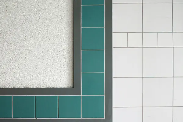 White square wall tile framed by a border of green tile around a window opening