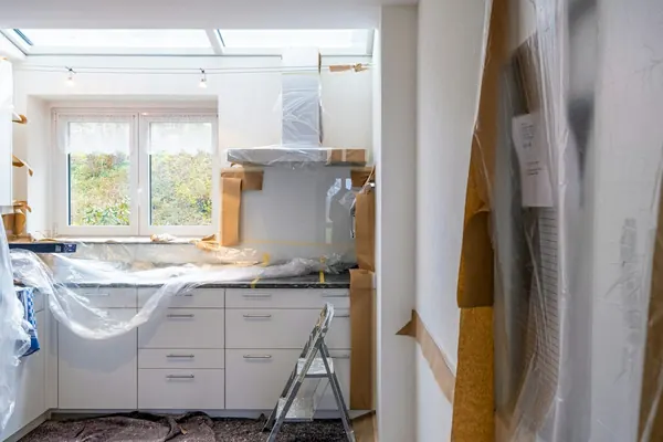 Kitchen mid-renovation with new white cabinets wrapped in plastic and brown paper