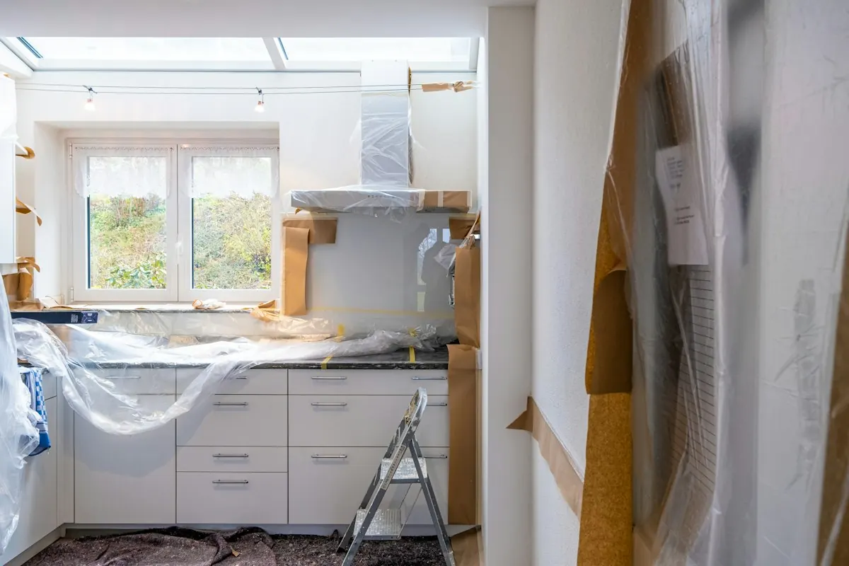 Kitchen mid-renovation with new white cabinets wrapped in plastic and brown paper