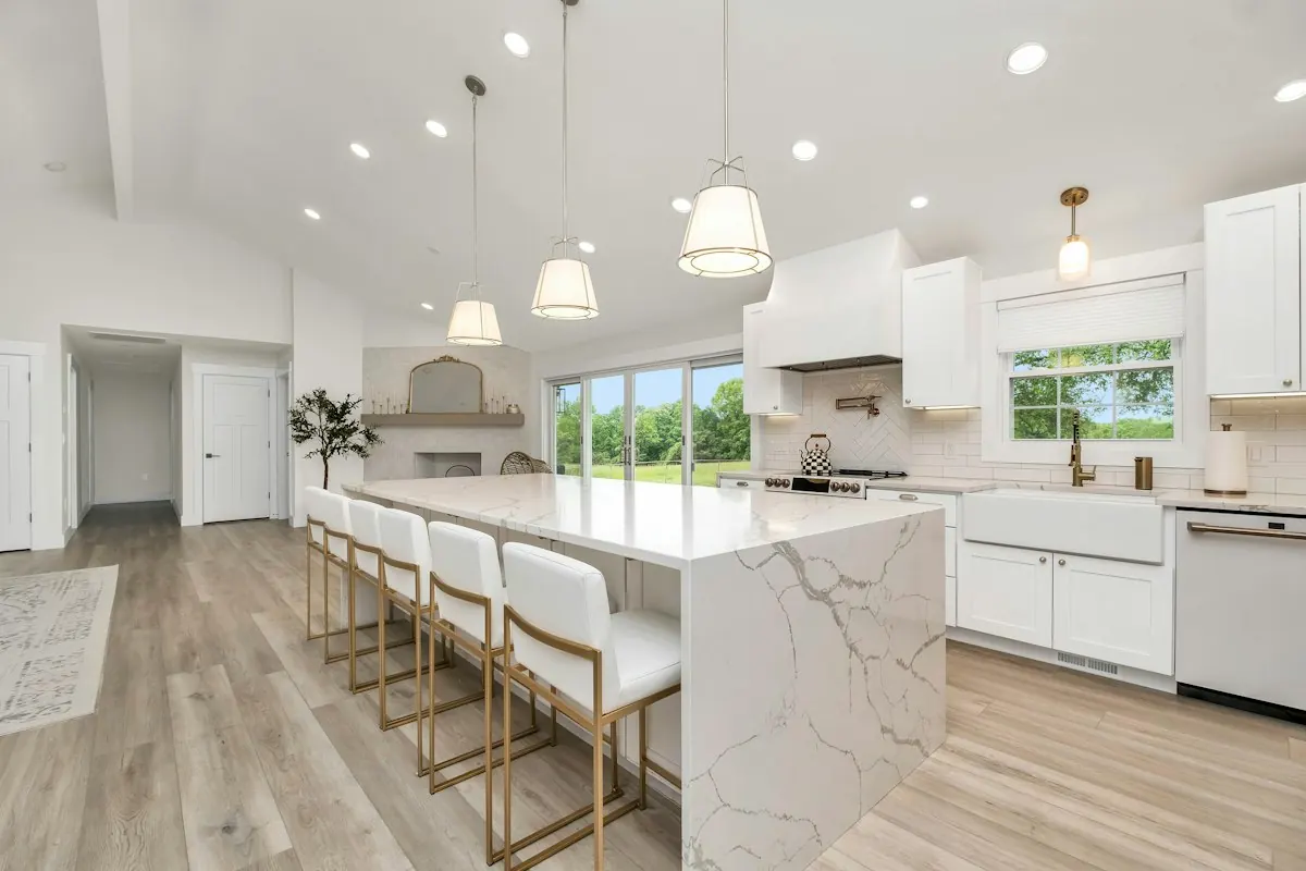 Open kitchen with a long marble waterfall island, bar stools and white cabinets