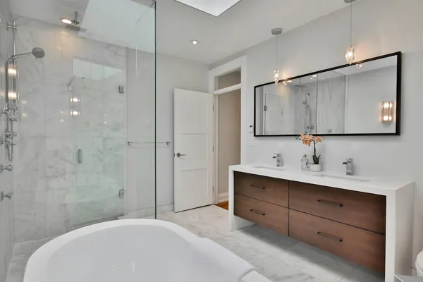 Marble-tiled walk-in shower and a freestanding tub with a walnut double vanity under a skylight