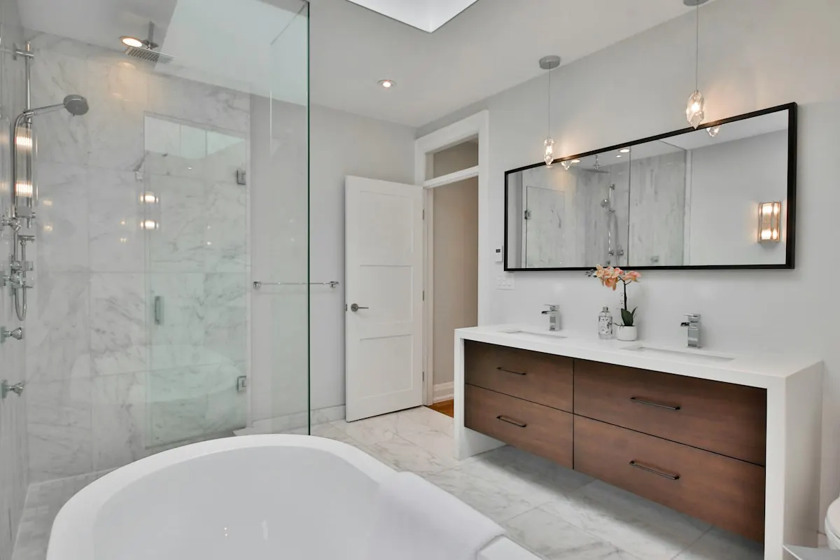 Marble-tiled walk-in shower and a freestanding tub with a walnut double vanity under a skylight