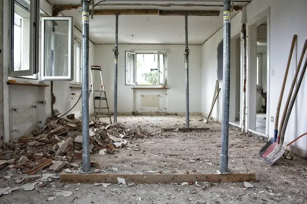 Gutted room with temporary steel shoring posts holding up the ceiling while a wall is removed