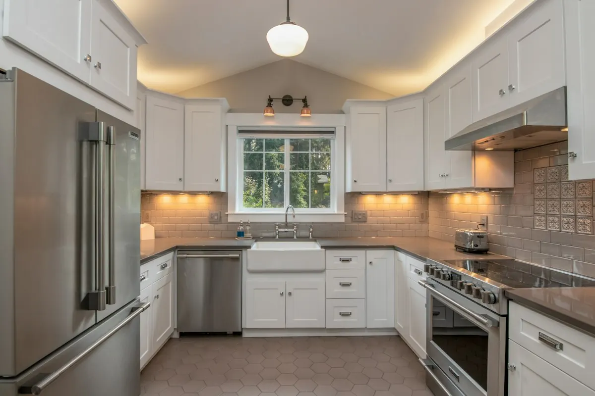 Compact U-shaped kitchen with white shaker cabinets, under-cabinet lights and a farmhouse sink under the window