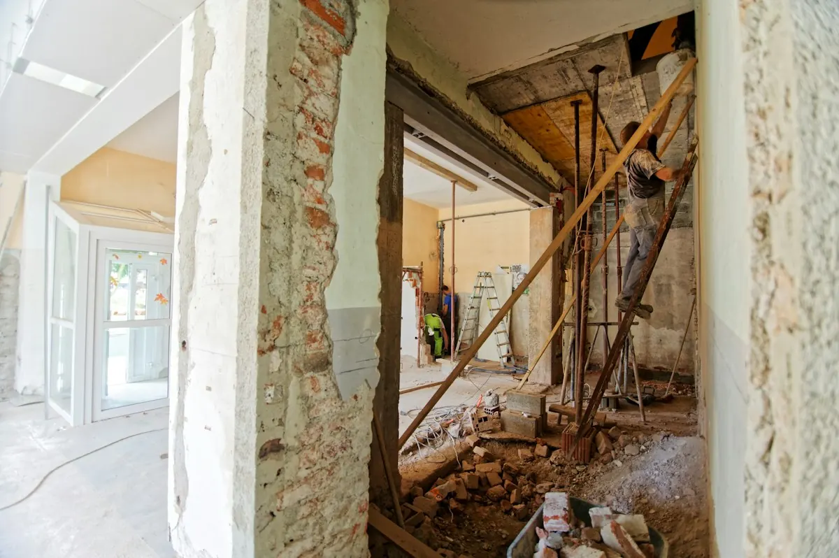 Worker on a ladder beside a wall opening cut through brick during an interior renovation