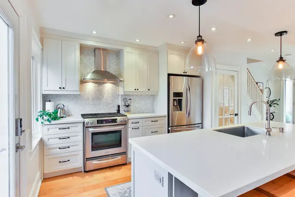 White kitchen cabinets with a quartz countertop, pendant lights and a stainless range