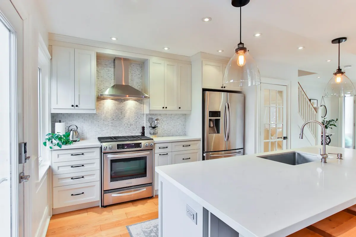 White kitchen cabinets with a quartz countertop, pendant lights and a stainless range