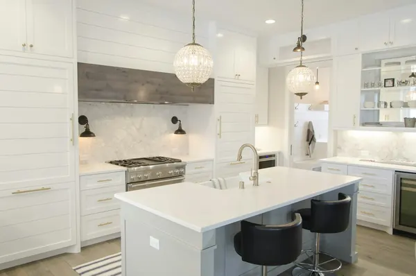 White kitchen with a large island, pendant lights and a range hood over a six-burner range