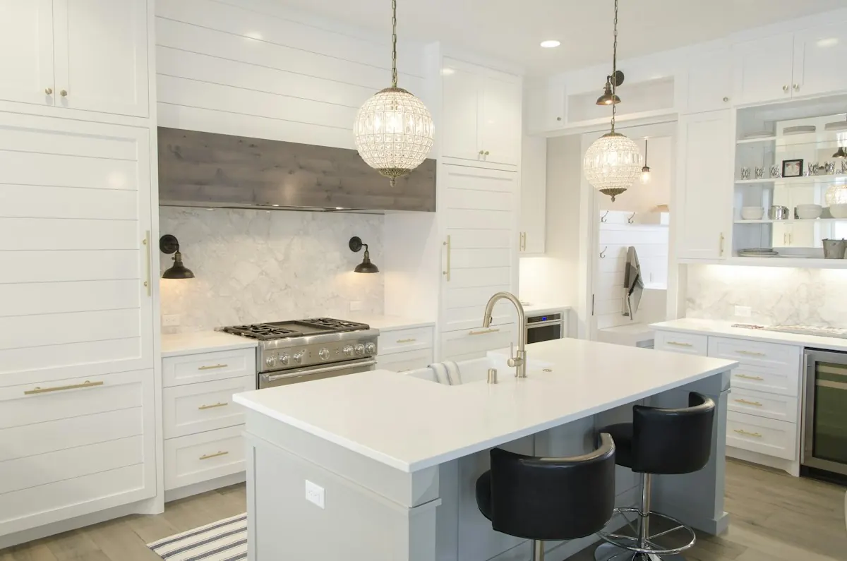 White kitchen with a large island, pendant lights and a range hood over a six-burner range
